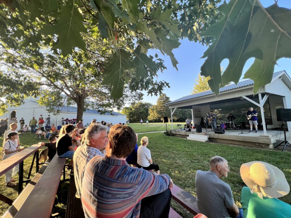 A crowd of people watches live music on the stage at the Vinland Fair.