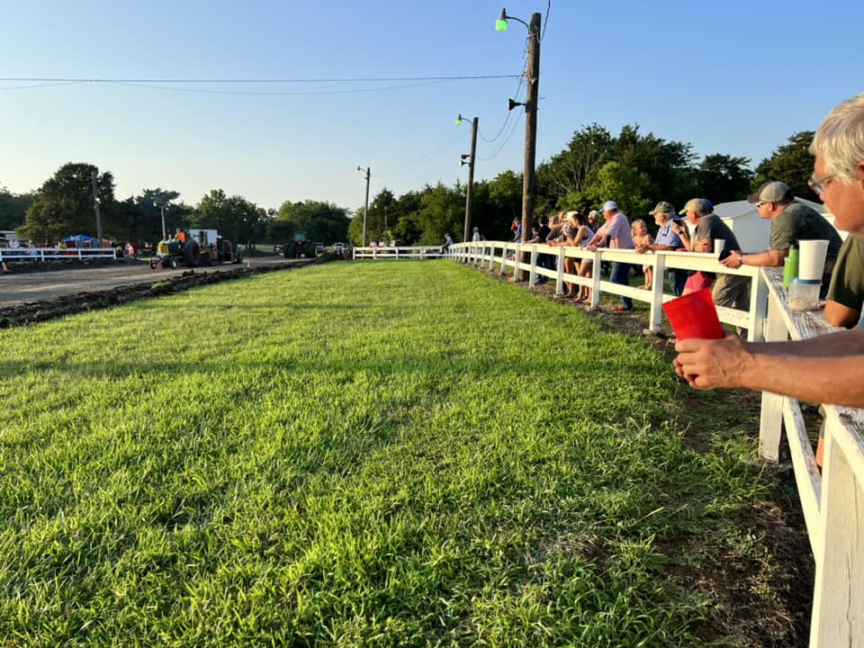 The audience watches the tractor pull from the fence.